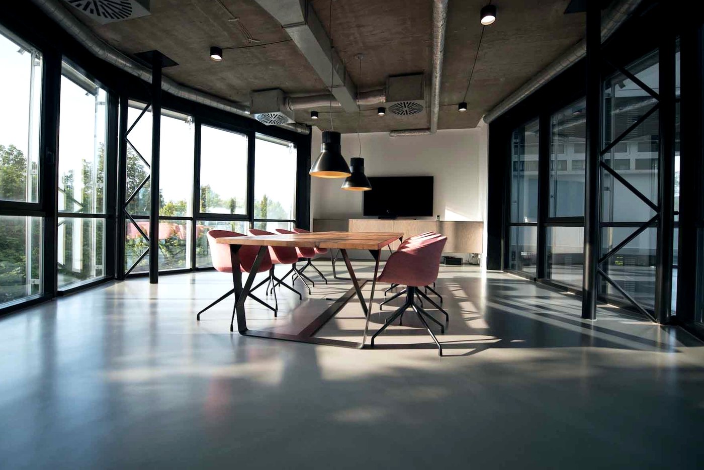 A long room with glass walls, a steel frame and a timber table with pink chairs